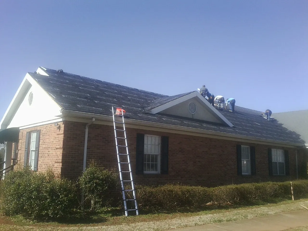 Crew tearing shingles off a brick ranch roof with a ladder set — Metal Roof Repair work by our crew in Walworth