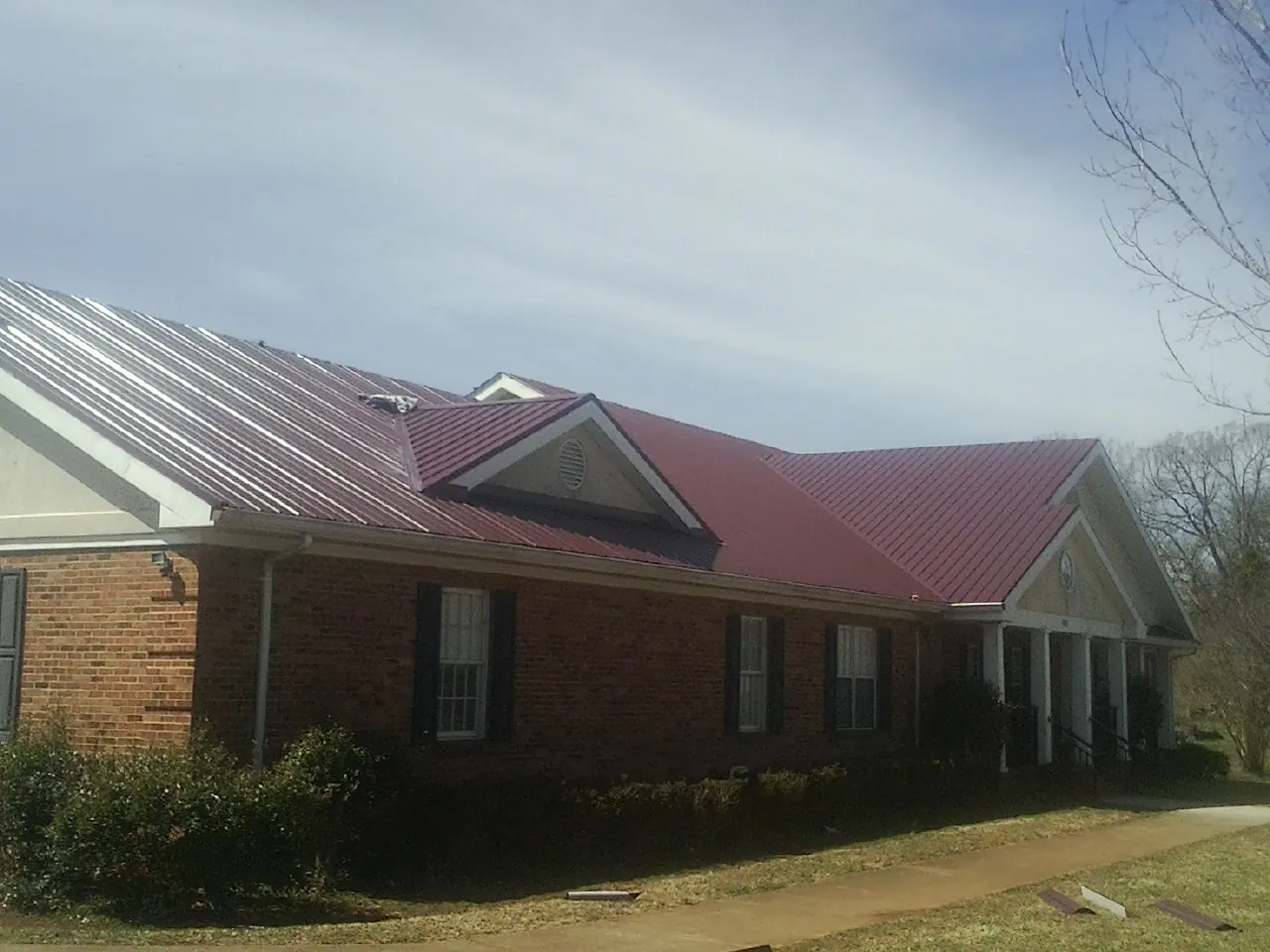 Red metal roof with gabled entries on a long brick building, from a Hail Damage Roof Repair job in Walworth