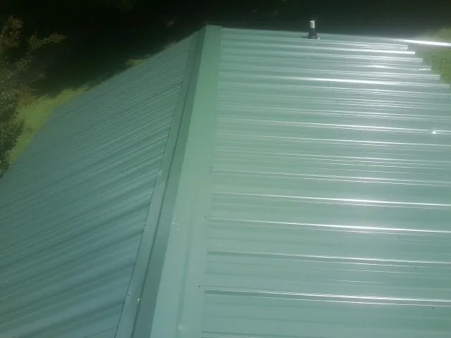 New green metal panels meeting at the ridge of a roof — Flat Roof Repair work by our crew in Walworth
