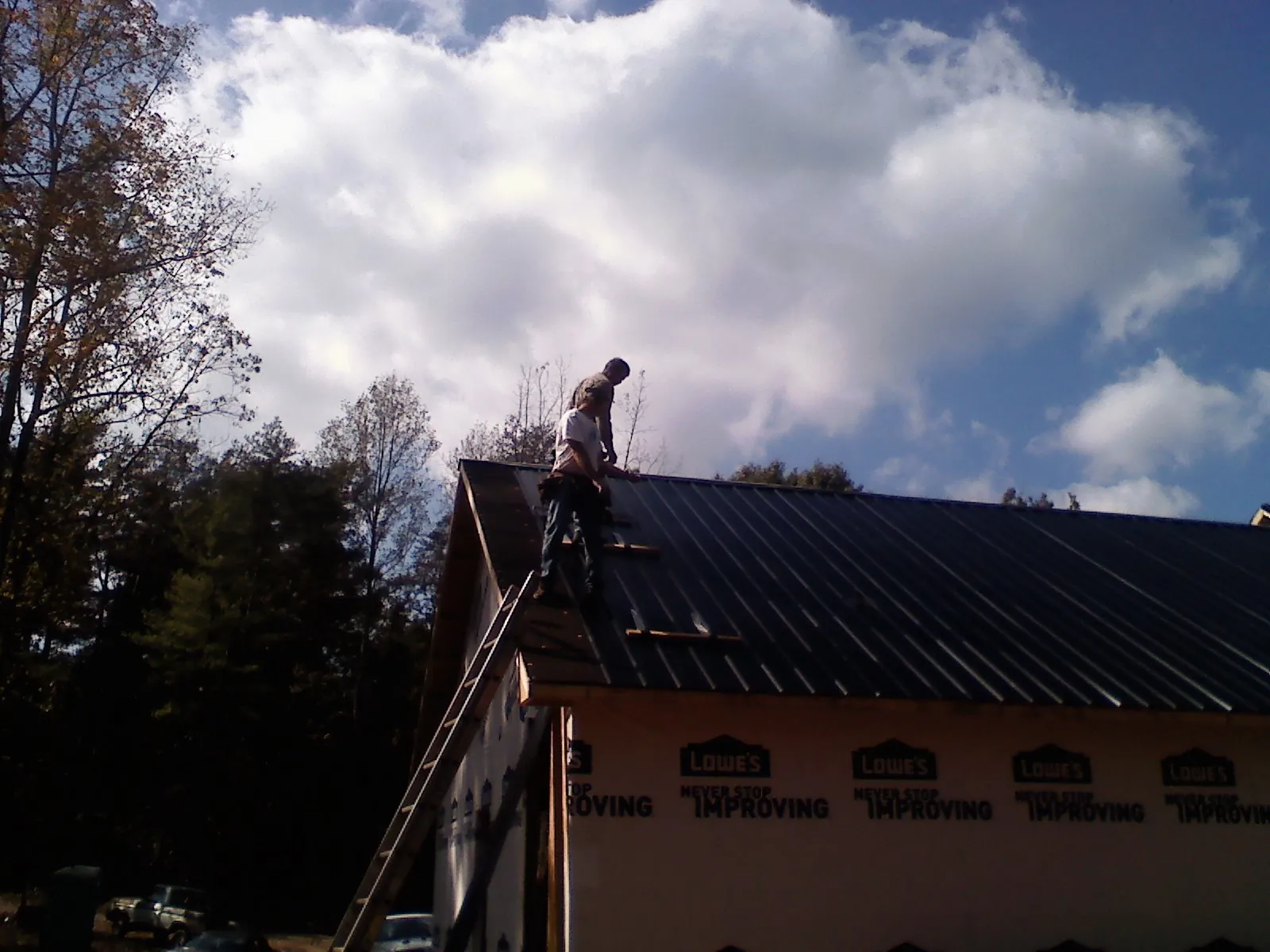 Roofer fastening dark metal panels high against a cloudy sky, from a Roof Inspection job in Walworth
