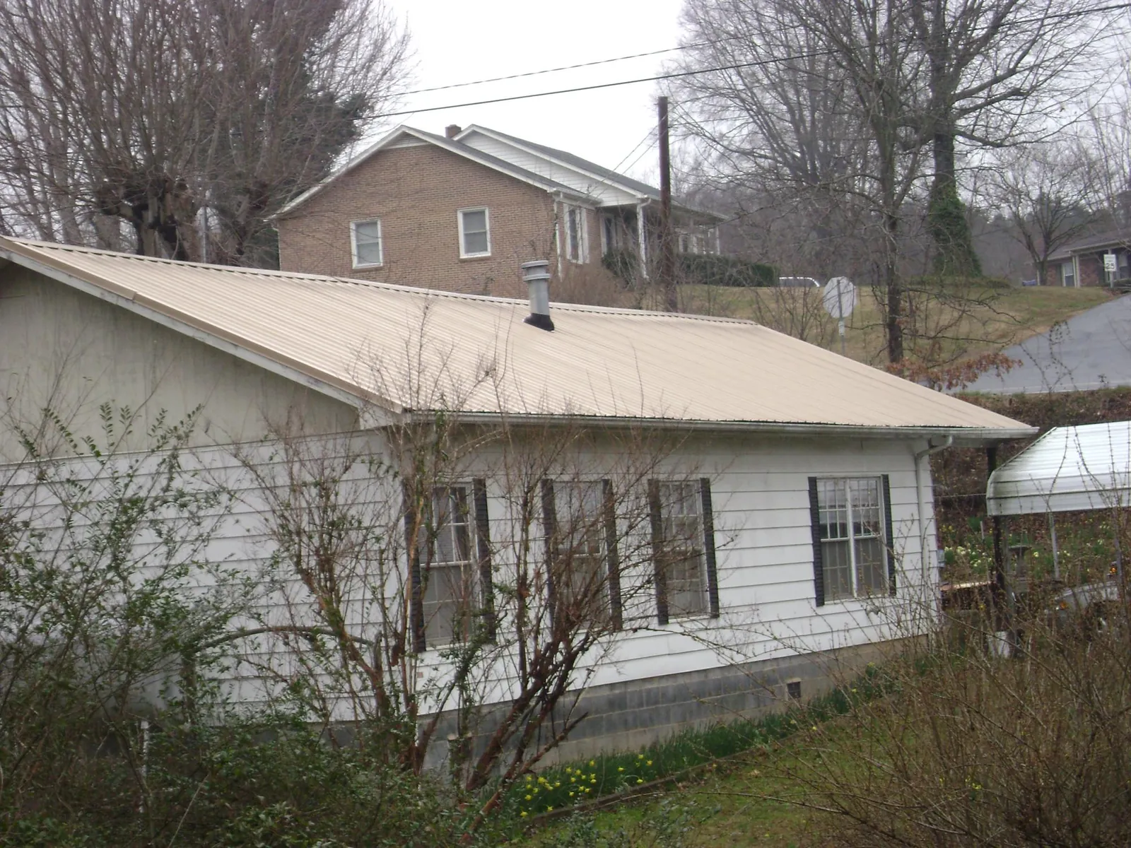 Tan metal roof on a white sided house set into a hillside — Commercial Roofing by Roofing Brothers in Walworth