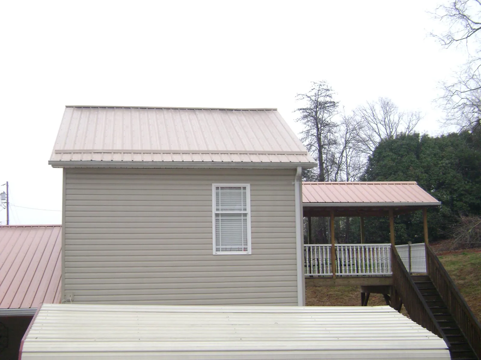Tan metal roofs on a two story addition and attached porch, from a Roof Replacement job in Walworth